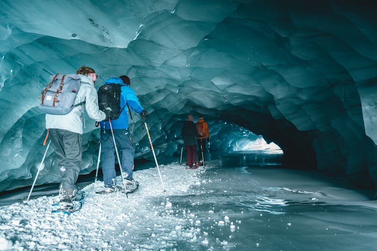 A group of adventurers hiking through a stunning blue ice cave in Zermatt, Switzerland.