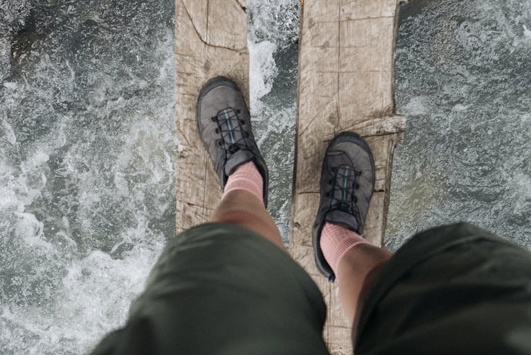 A hiker crosses a rustic wooden bridge over a rushing river, capturing adventure and exploration.