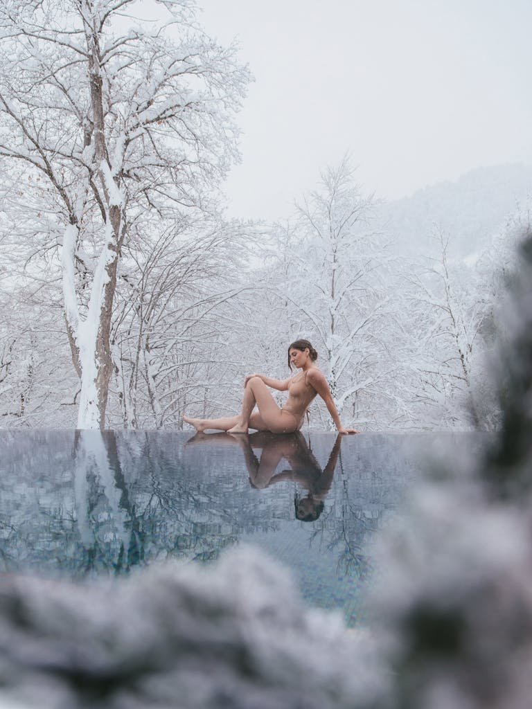 A woman enjoys the calm of an infinity pool amidst snow-covered trees in winter.