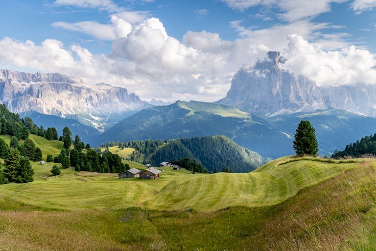 Idyllic landscape in the Dolomites, Italy with lush green fields and majestic mountains under a blue sky.