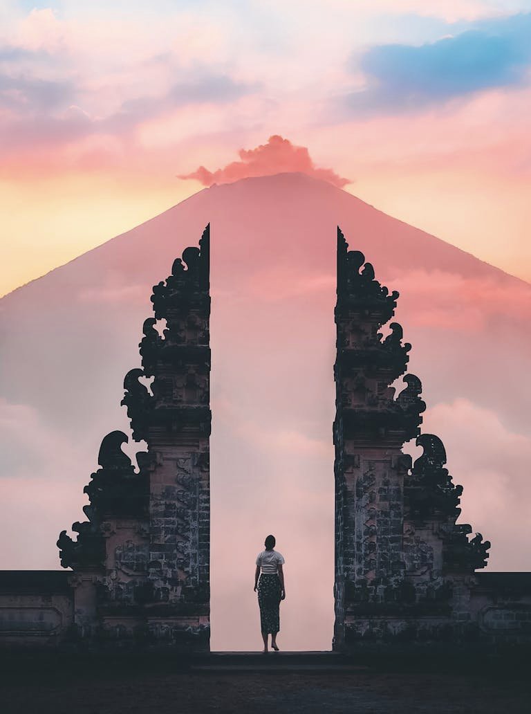 Serene sunrise view of a person standing at Lempuyang Temple's gateway, Bali, Indonesia.